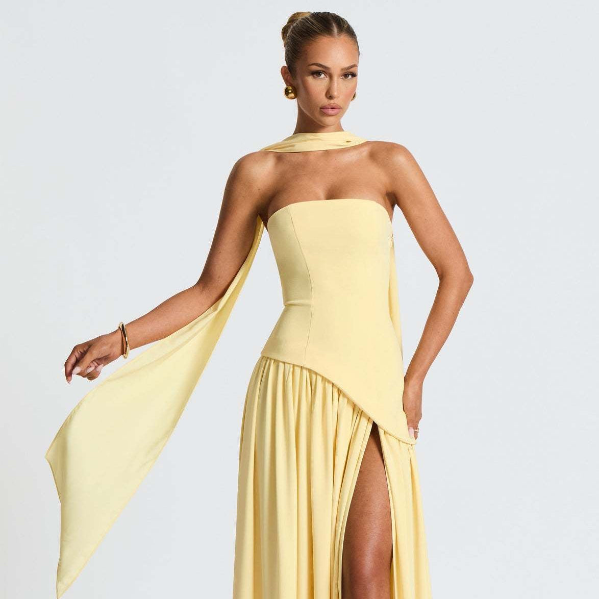 Woman wearing a yellow evening gown with a slit on a white background