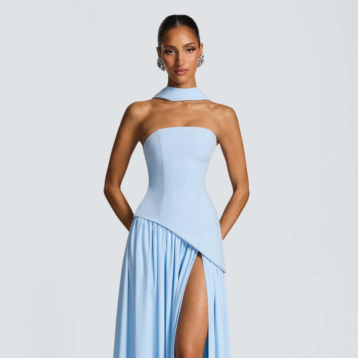 Woman wearing a light blue strapless gown with a slit on a white background