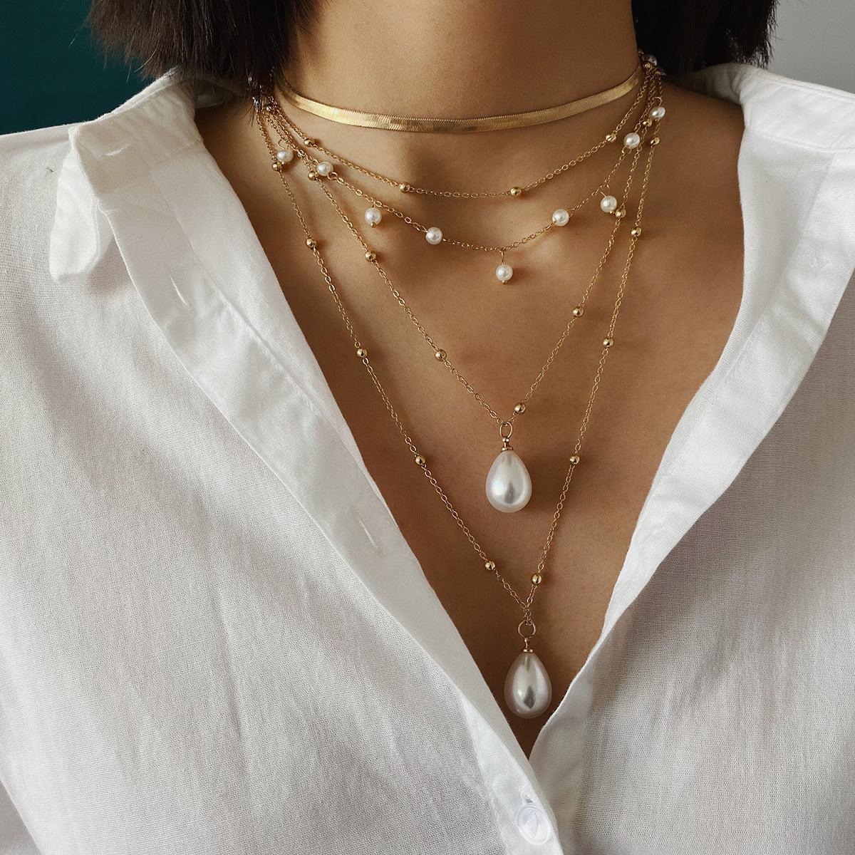 Close-up of a person wearing multiple gold necklaces with pearls on a white shirt.