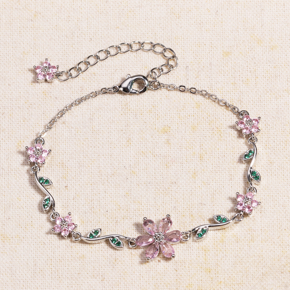 Silver bracelet with pink flower-shaped charms on a beige fabric background