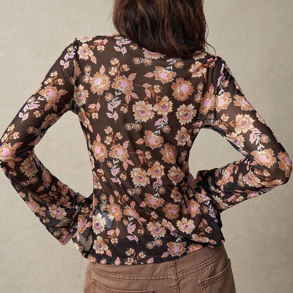 Person wearing a floral blouse with long sleeves and brown pants against a neutral background